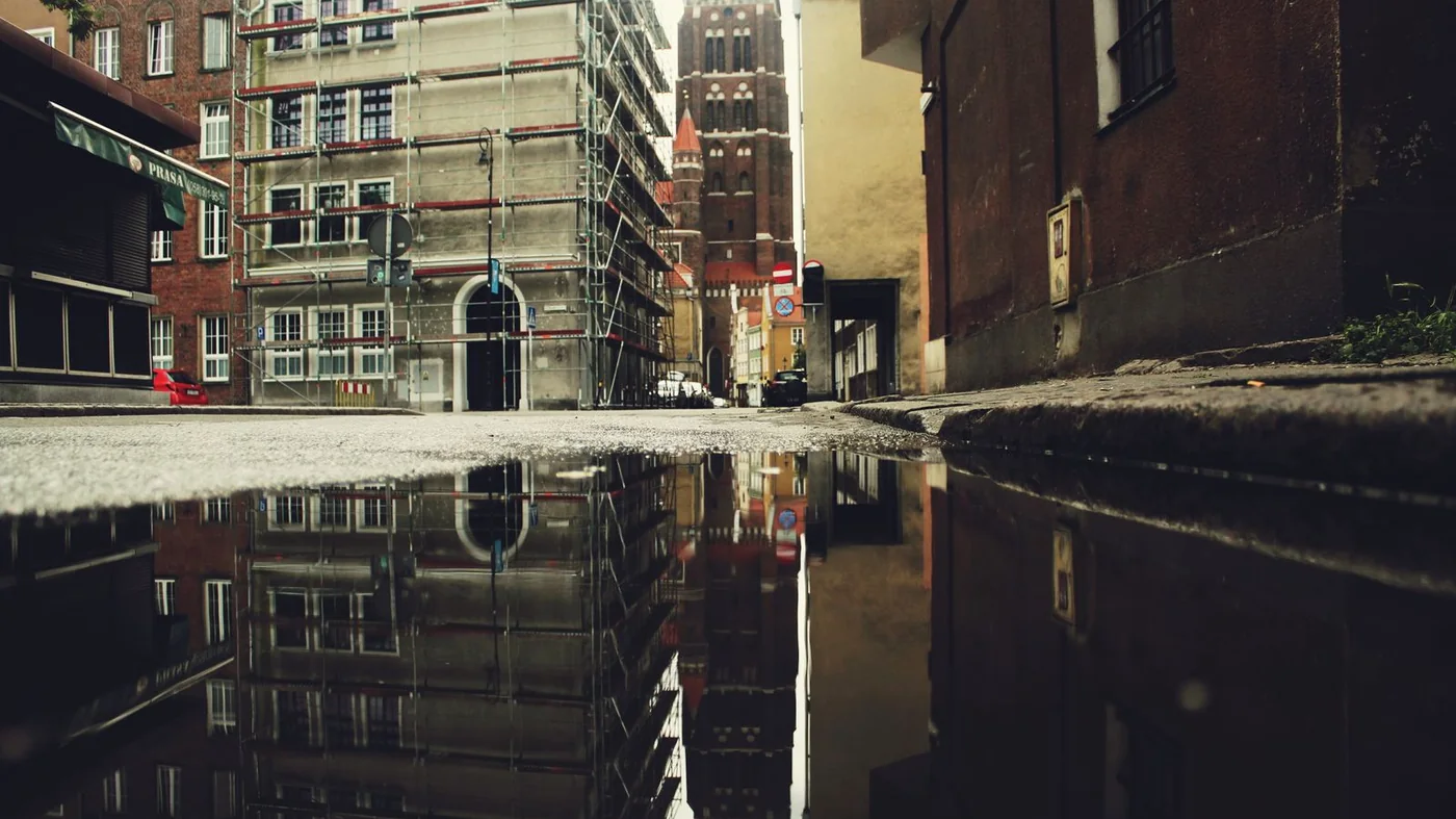 Grote plas water op straat na een regenbui, met weerspiegeling van de gevels
